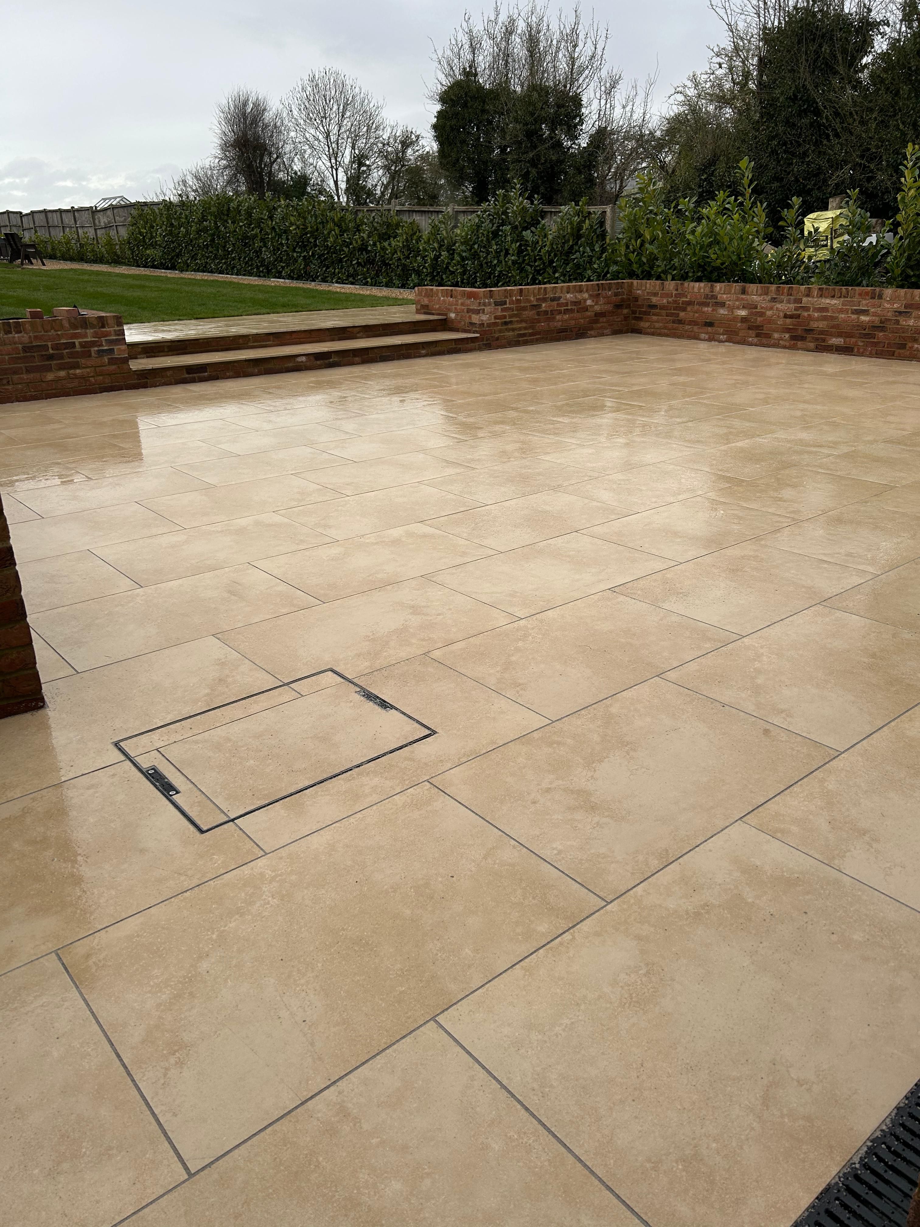 A finished pale-stone patio with brick raised beds, broad steps and a green lawn at a Progreen garden project